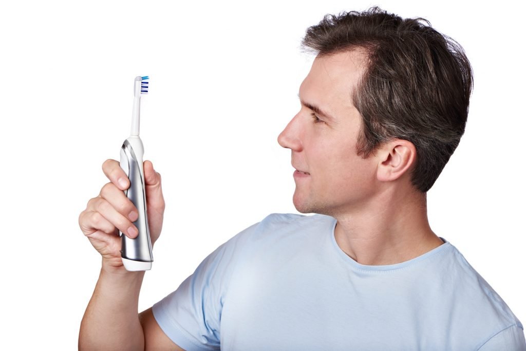 Happy man looks at electric toothbrush isolated